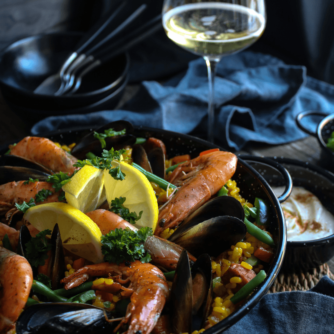 Paella med saffransris, räkor, musslor, kyckling och grönsaker i en bred panna.