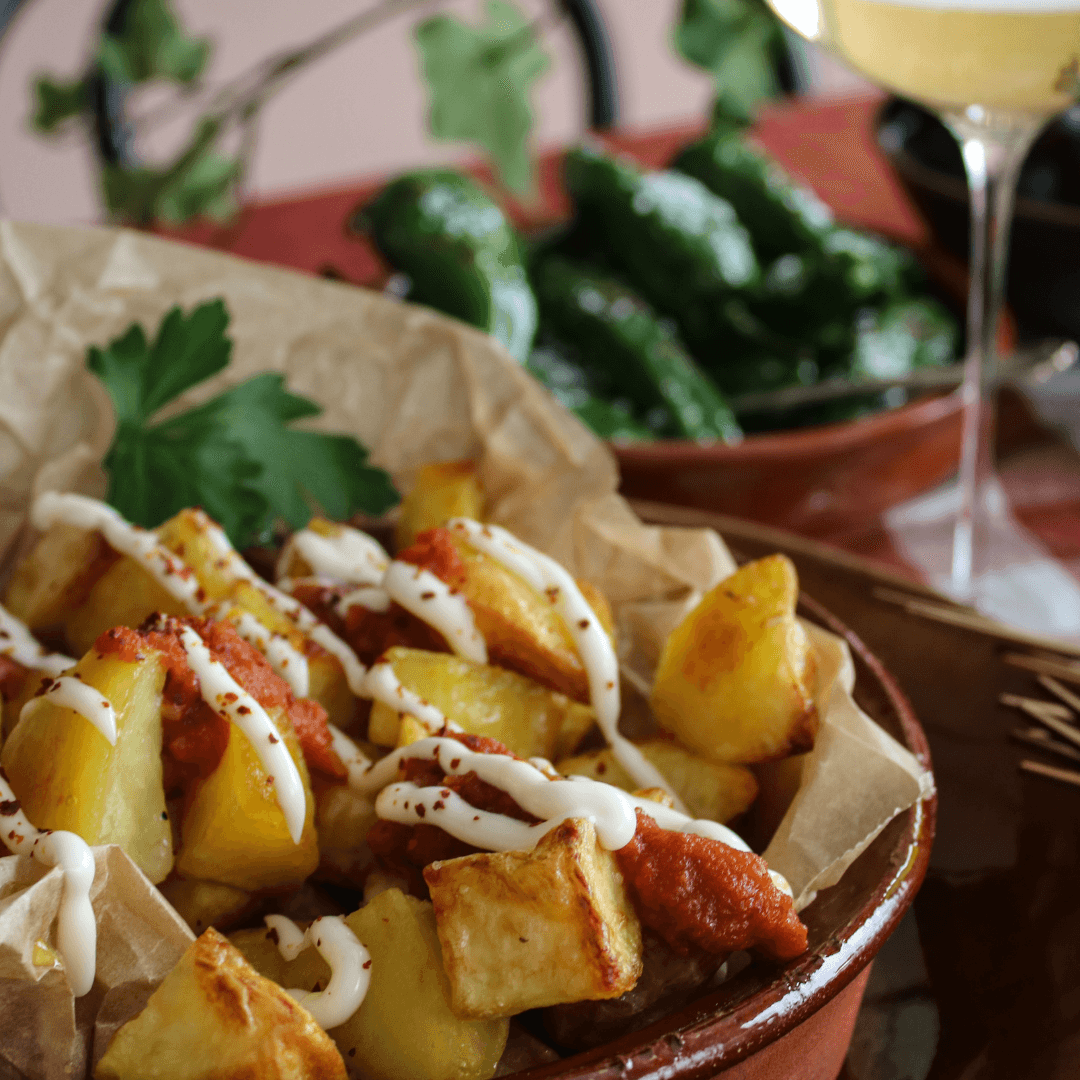 Krispiga gyllenrostade potatisbitar serverade med röd bravasås och krämig aioli i små skålar.