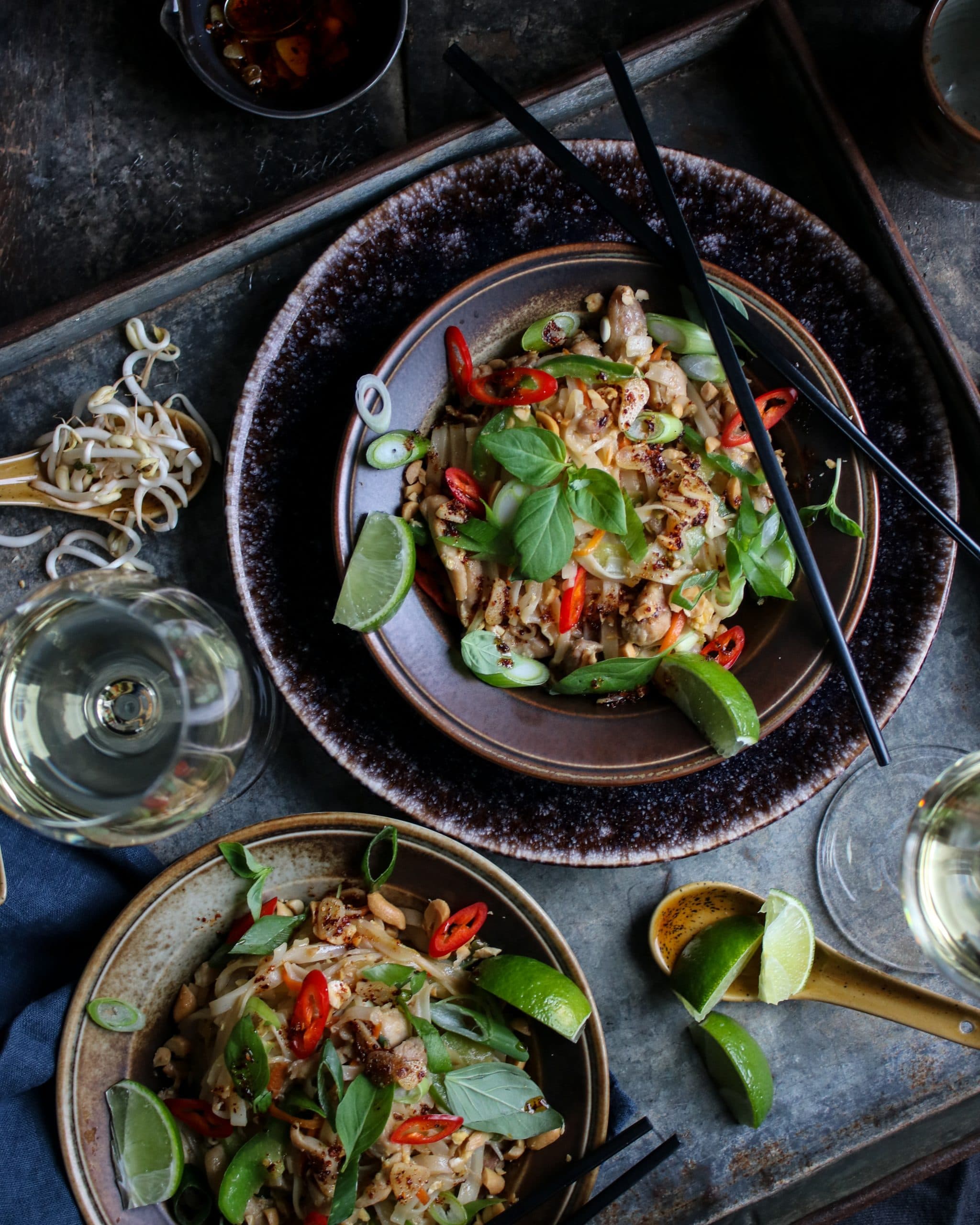 Pad Thai med kyckling och crispy chilioil med en mörk dukning och ett glas vitt halvtorrt vin.
