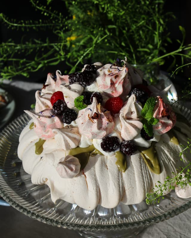Påskpavlova med krämig fyllning, pistagenötter och färska bär.