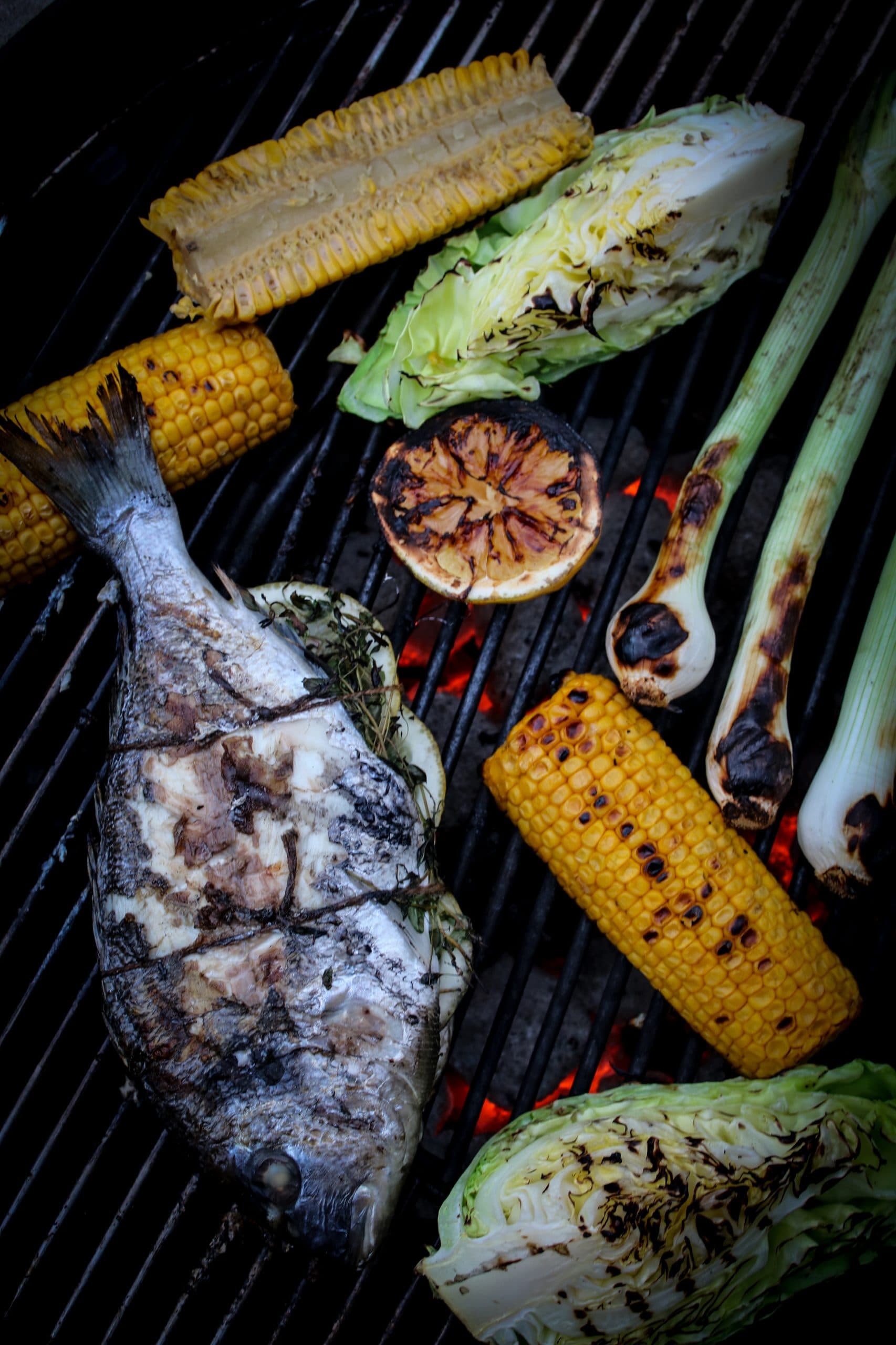 Hel grillad fisk fylld med citron och örter, serverad med grillade grönsaker och grön dressing.
