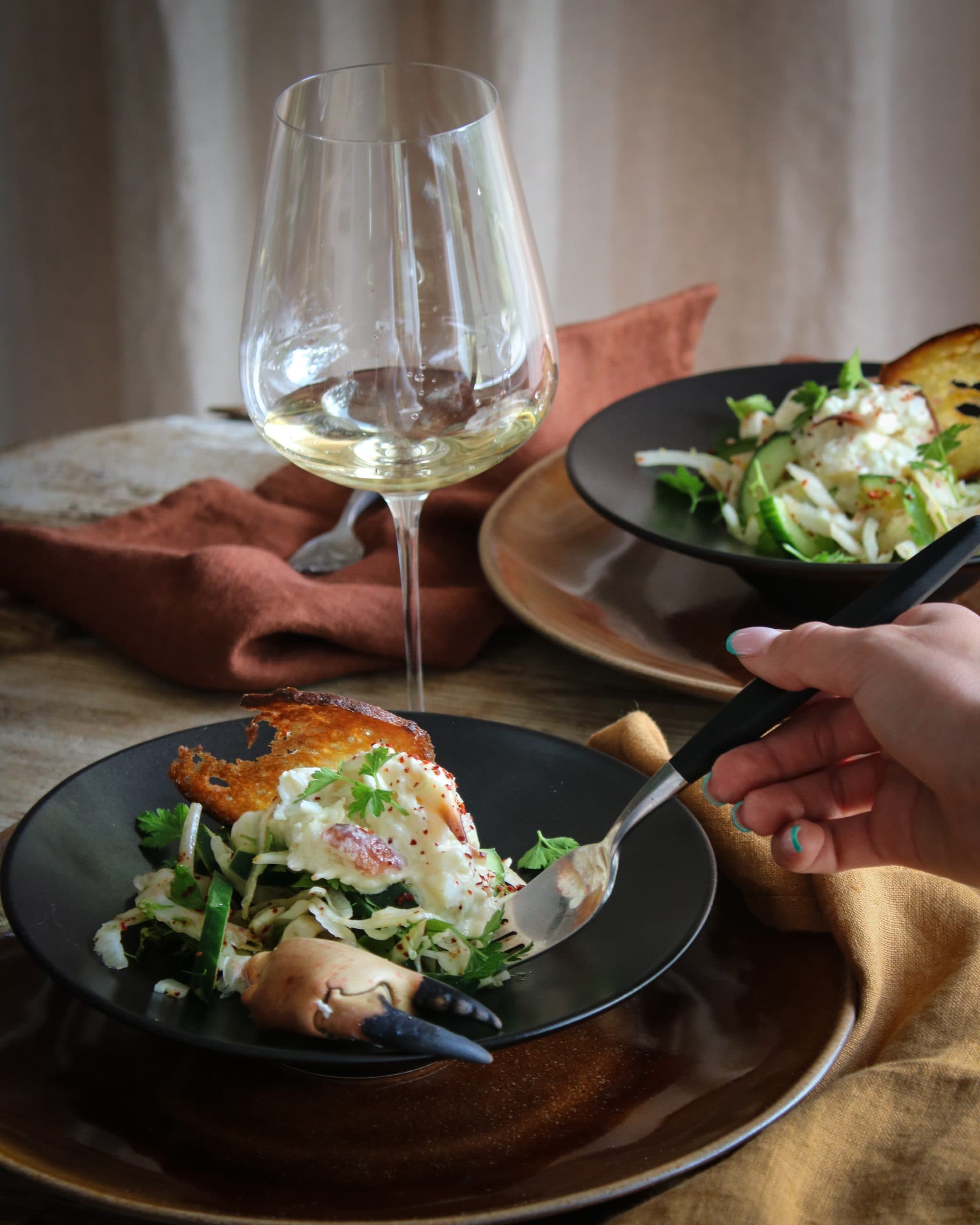 Sallad med krabba och fänkål med en vacker dukning i mörkt tema. Serveras med ett glas vitt.